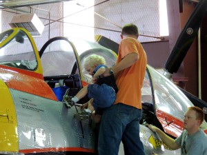 Under the watchful eye of Alan Haskin, a museum visitor helps his son get an up close and personal look at the T-28 cockpit.