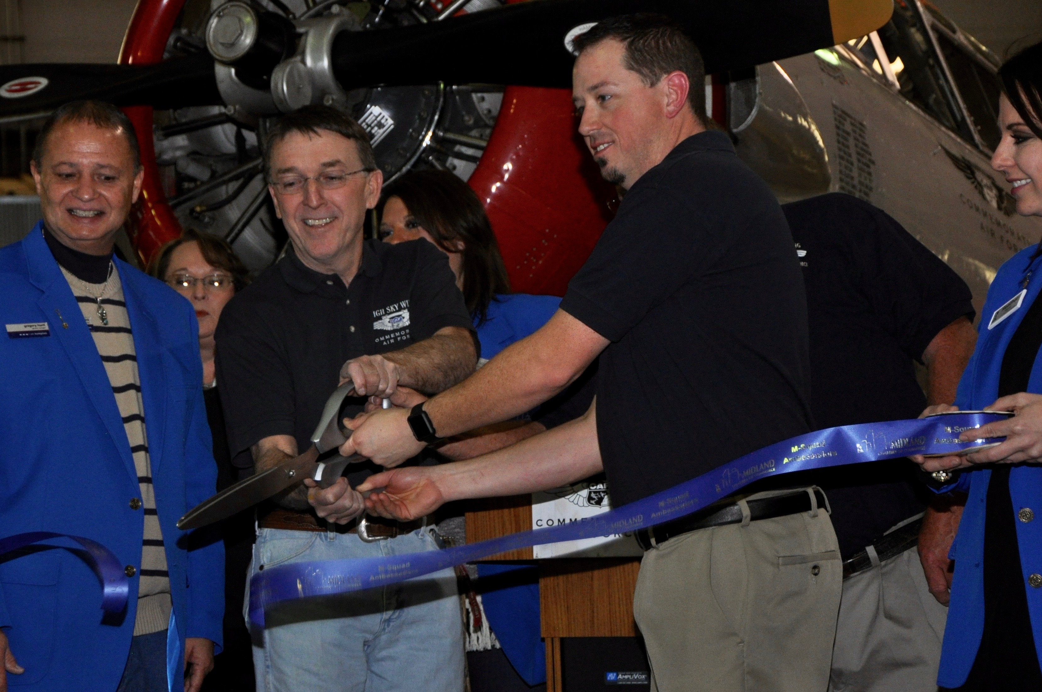 As Midland Chamber of Commerce members look on, Brent Collins, Mark Haskin (hidden) and Michael Clinton cut the ribbon officially opening the Midland Army Air Field Museum.